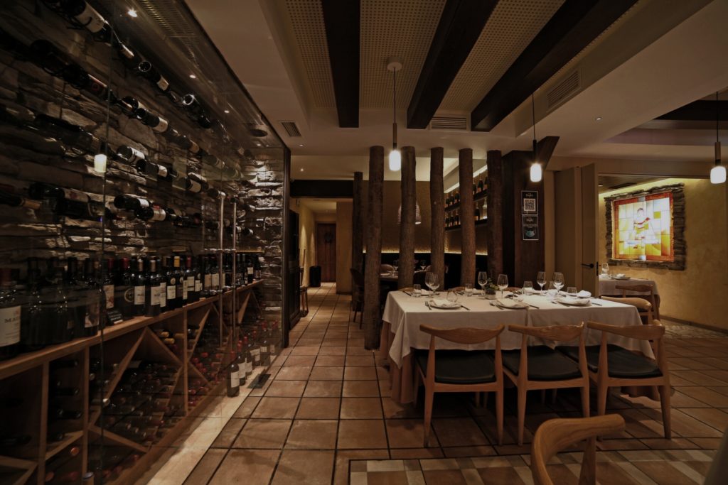 Tienda de vinos con paredes de botellas y mesa de madera, proyecto retail por Klic Arquitectos