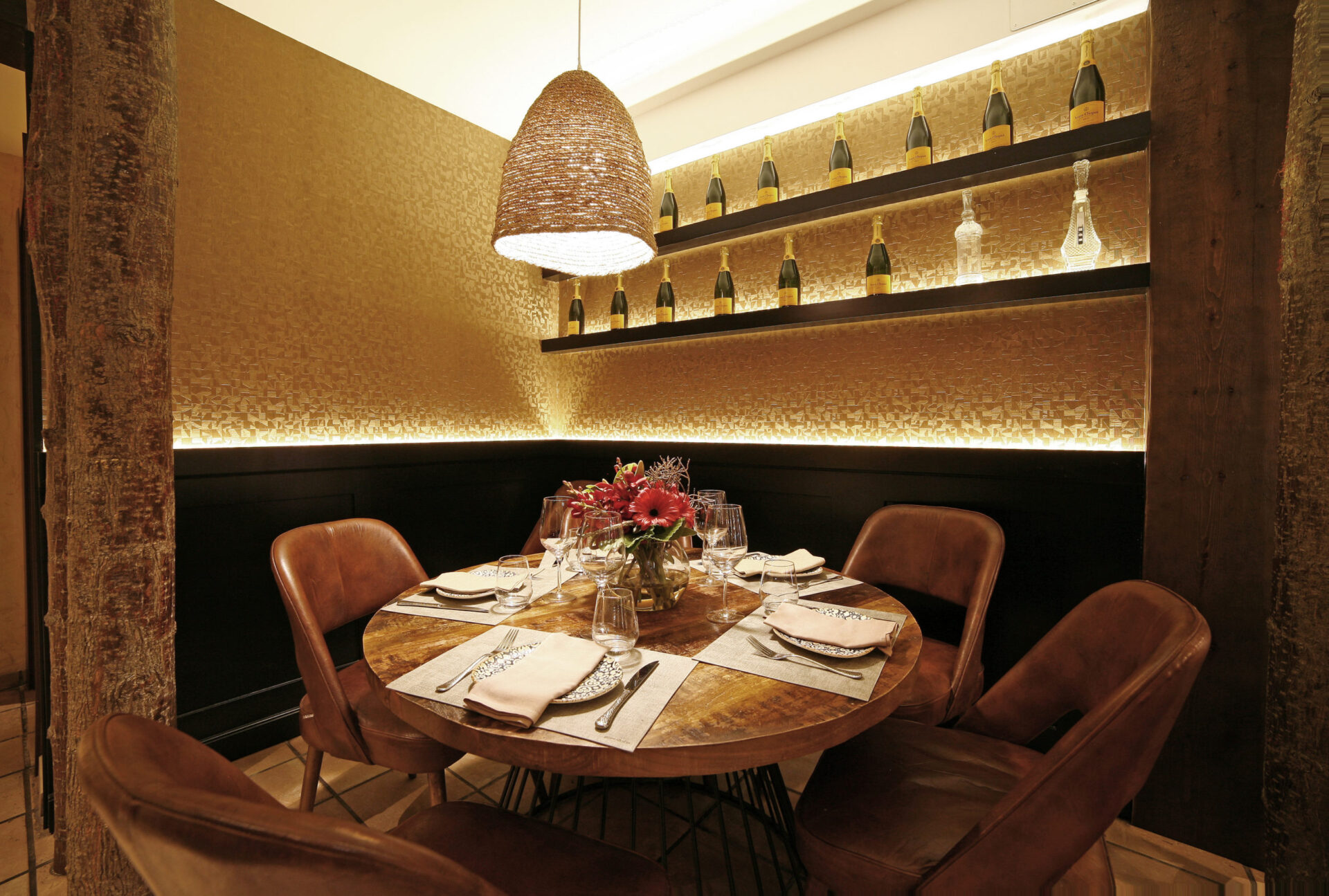 Separee des Asador Iñaki in der Calle Ayala, Málaga mit hinterleuchtetem Champagner-Display, rundem Holztisch und Vintage-Ledersesseln von Klic Arquitectos