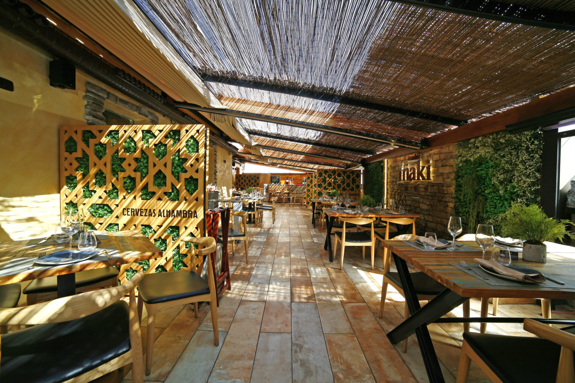 Außenterrasse des Asador Iñaki in der Calle Ayala, Málaga mit Schilfrohrdecke, nasridischen Gitterwerken mit Vegetation und Iñaki-Logo in vertikalem Garten von Klic Arquitectos