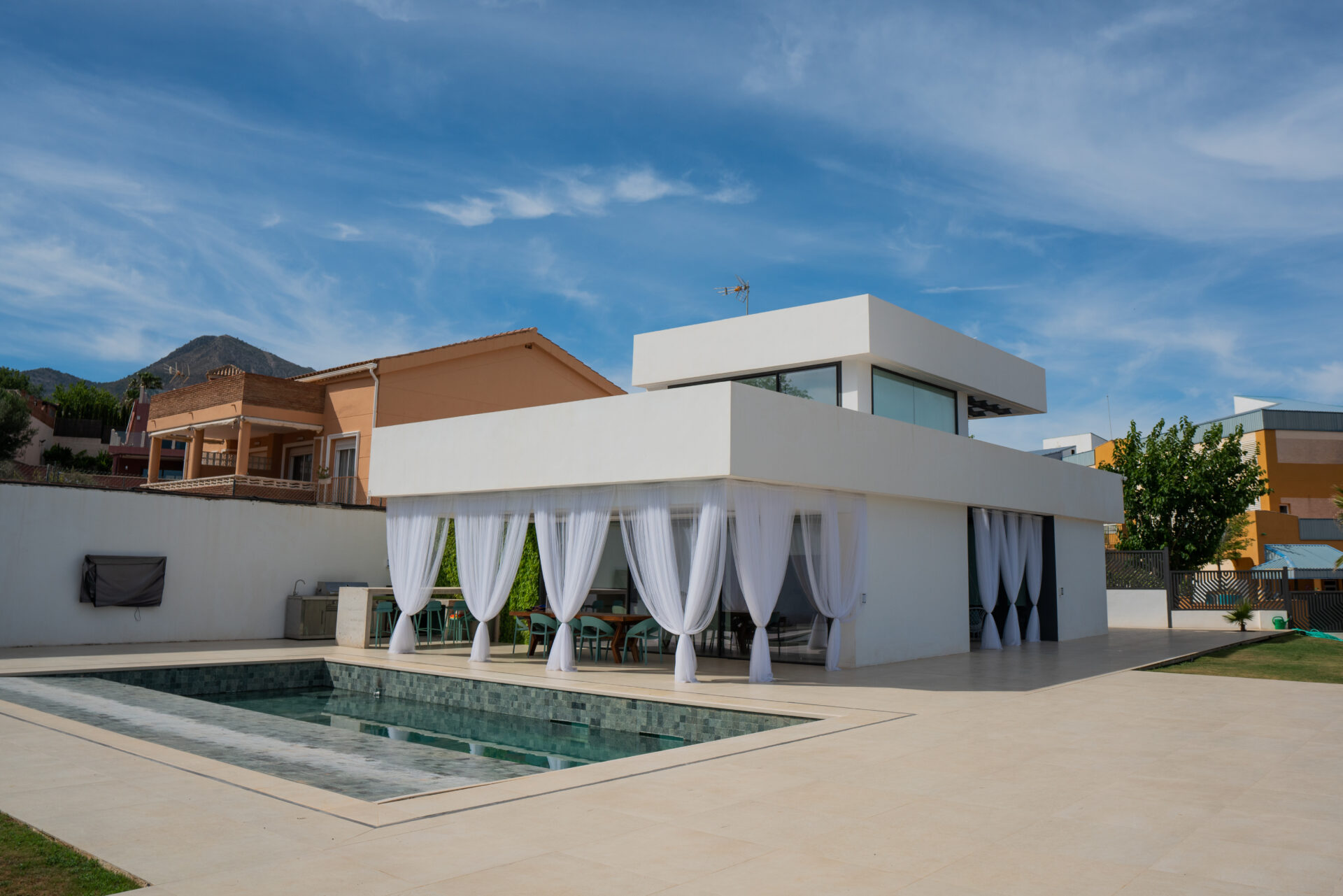Fachada principal con piscina y cortinas blancas de Casa Maravillas en Benalmádena Costa (Málaga) por Klic Arquitectos