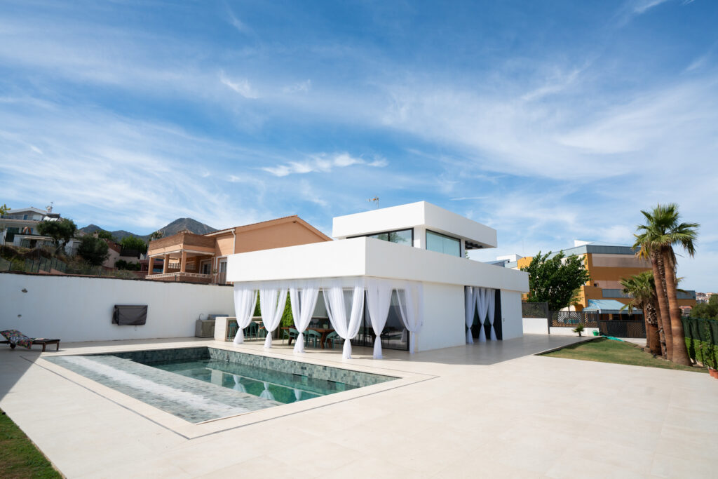 Vista del conjunto exterior con piscina y porche con cortinas en Casa Maravillas (Benalmádena, Málaga), vivienda de Klic Arquitectos
