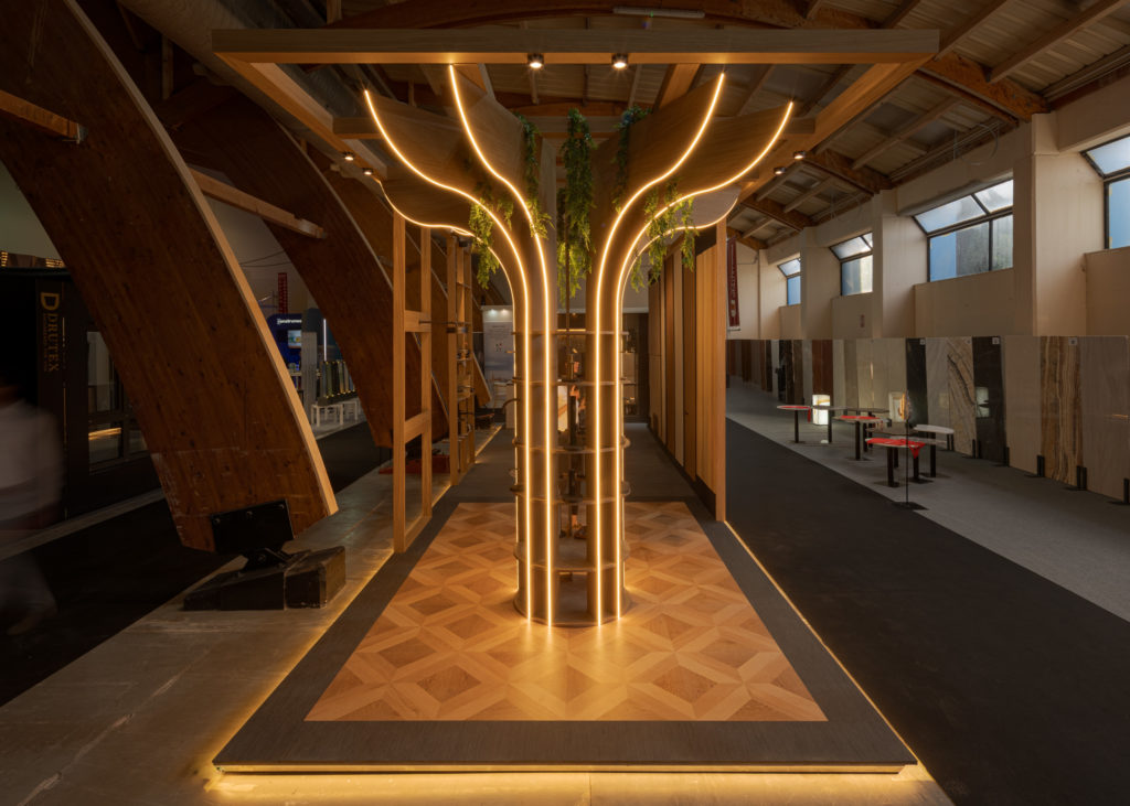 Gesamtansicht des Stands El Santuario auf dem Marbella Home Meeting 2026 mit LED-Baumsäule und Holzbögen, von Klic Arquitectos