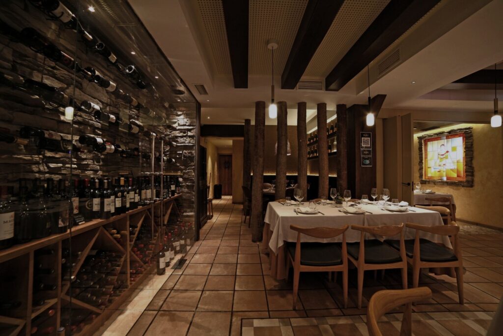 Tienda de vinos con paredes de botellas y mesa de madera, proyecto retail por Klic Arquitectos