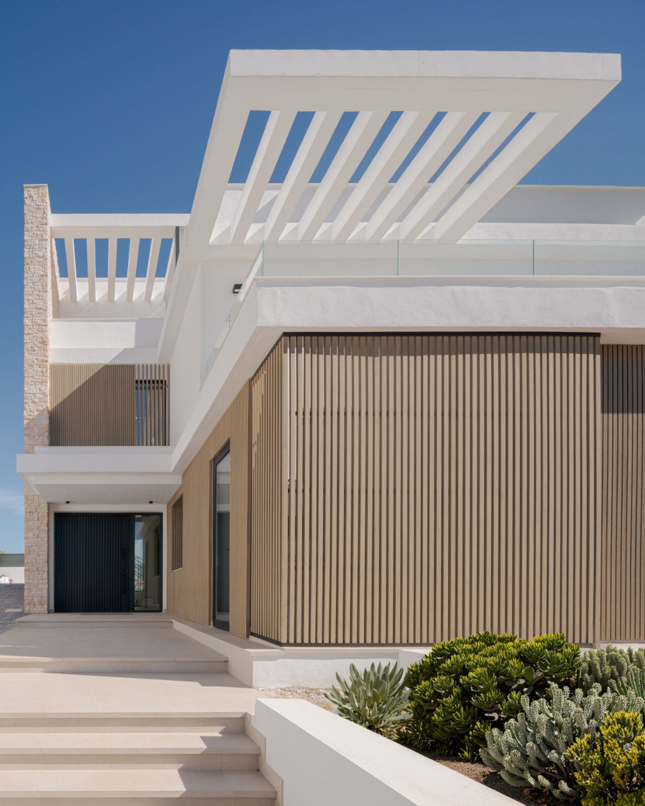 Fachada con celosía de madera vertical y voladizos blancos en Villa Cártama, vivienda contemporánea en Cártama (Málaga) por Klic Arquitectos